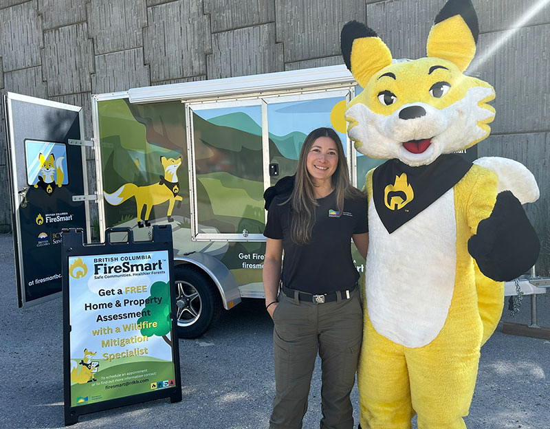 Carlene Pires, RDKB Emergency Program Coordinator and FireSmart Coordinator, with Ember the FireSmart Fox and the FireSmart Trailer on Wheels.